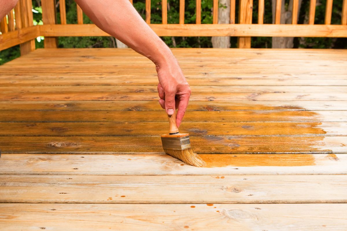 hand applying deck stain with a large paint brush